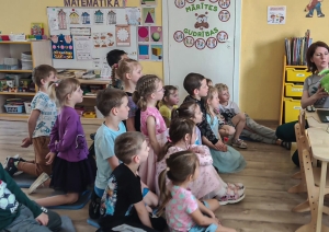 bērni sēž grpiņā, skatās datorā un klausās Jūlijas stāstu 