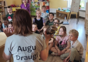 Jūlija ar muguru, bērni sēž aplīti un klausās