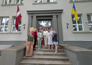 Latvijas un Ukrainas kolēģi stāv uz kāpnēm pie Valsts augu aizsardzības dienesta ieejas, fonā Latvijas un Ukrainas karogi