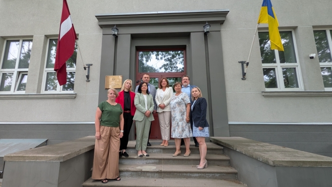 Latvijas un Ukrainas kolēģi stāv uz kāpnēm pie Valsts augu aizsardzības dienesta ieejas, fonā Latvijas un Ukrainas karogi