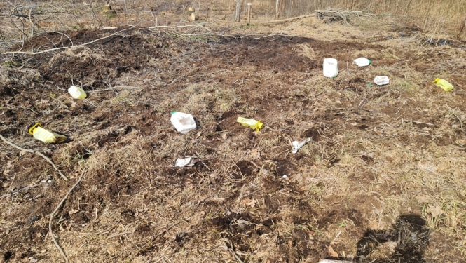 Laukums meža ielokā, kur redzmas izmētātas plastmas kanniņas
