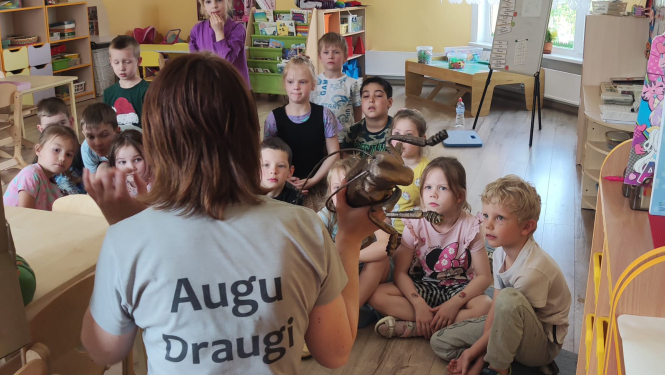 Jūlija ar muguru, bērni sēž aplīti un klausās