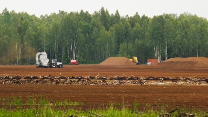 Uzarts klajš lauks, tālumā notiek mēslošana ar lauksaimniecības tehniku