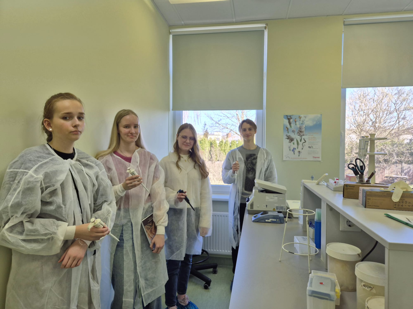 četri jaunieši - trīs meitenes un pusis stāv laboratorijā