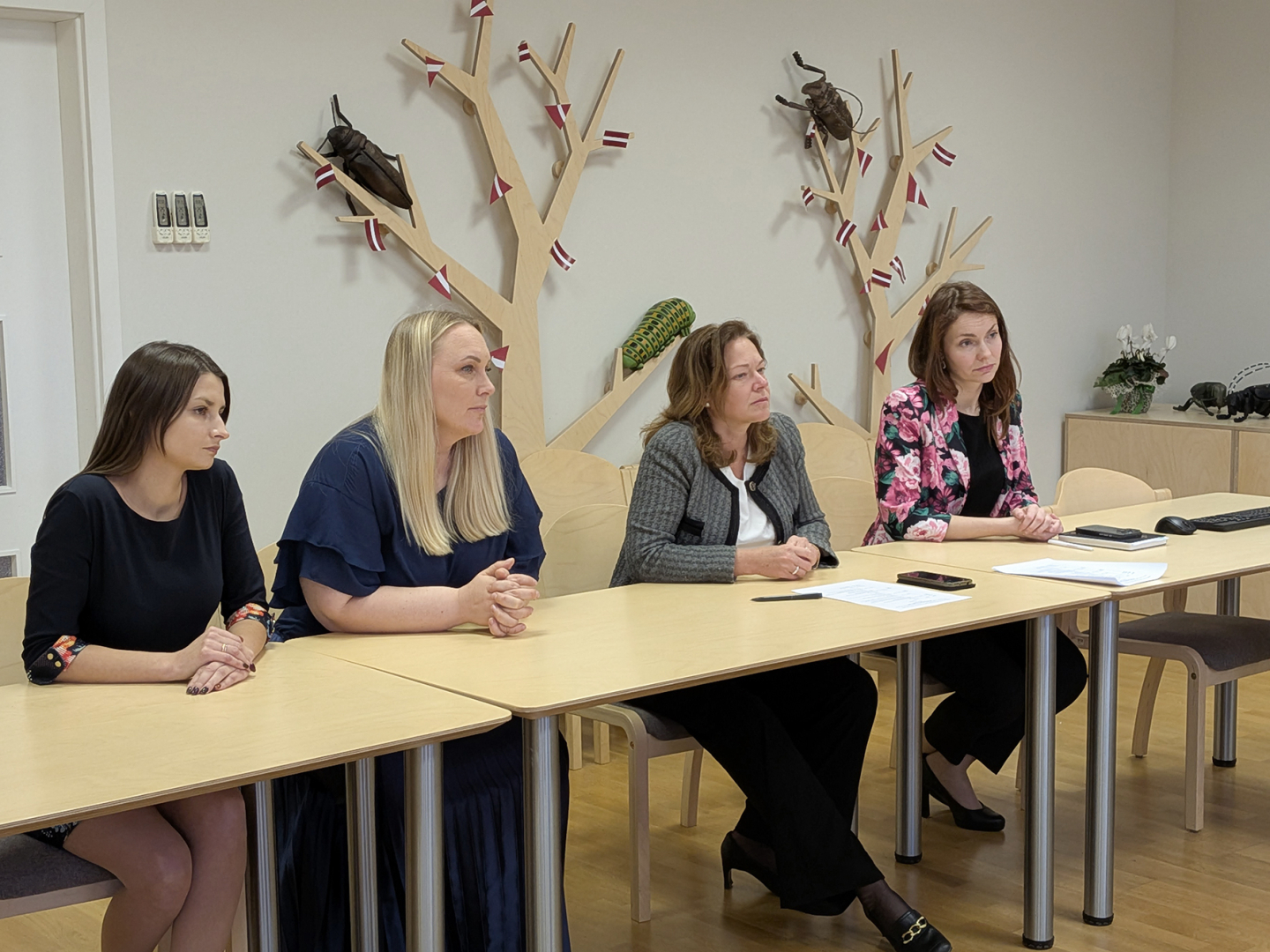 Sanāksmju zālē pie galda VAAD amatpersonas, fonā pie sienas dekors koka formā ar kukaiņu maketiem