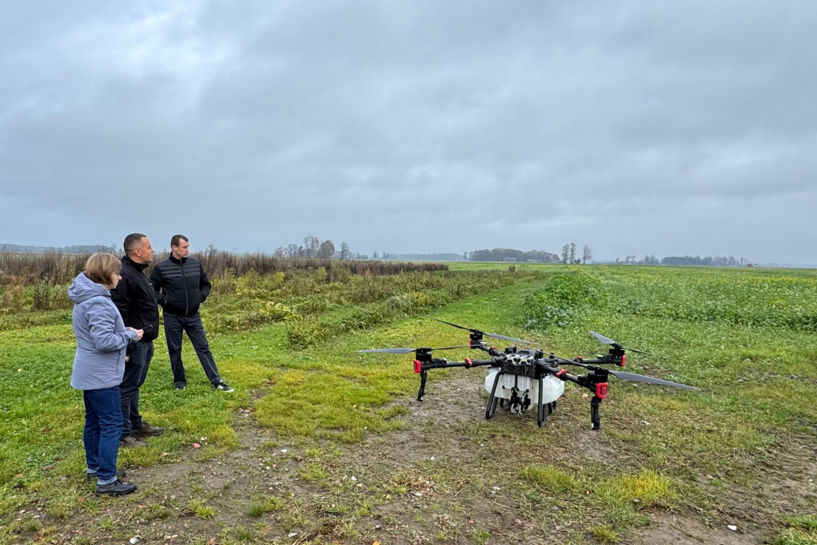 Atklāts lauks, 3 cilvēki lauka malā un drons