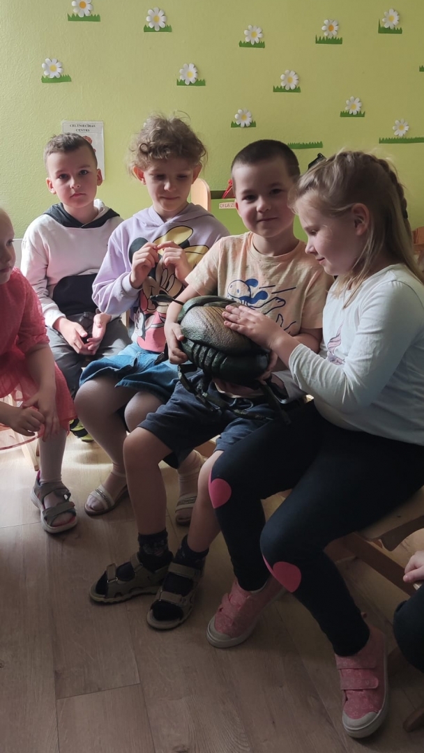 Bērni tur rokā kukaiņu maketu un pēta