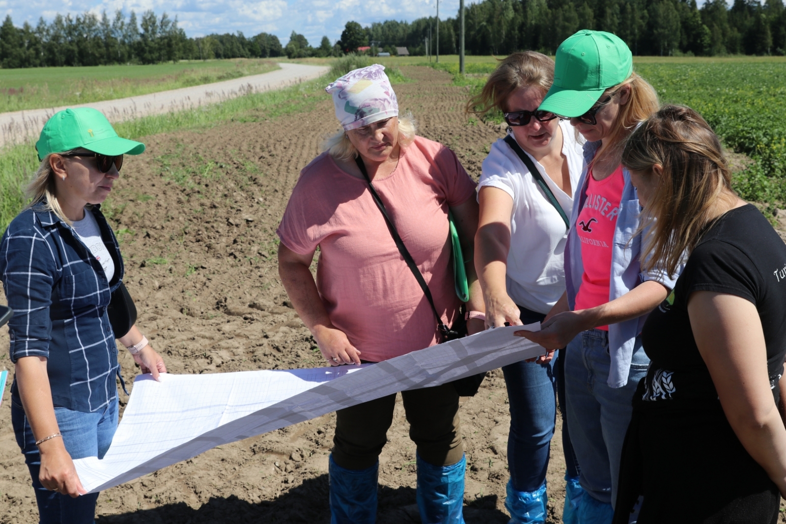 uz lauka cilvēki skatās lielā plakātā, ko tur rokās