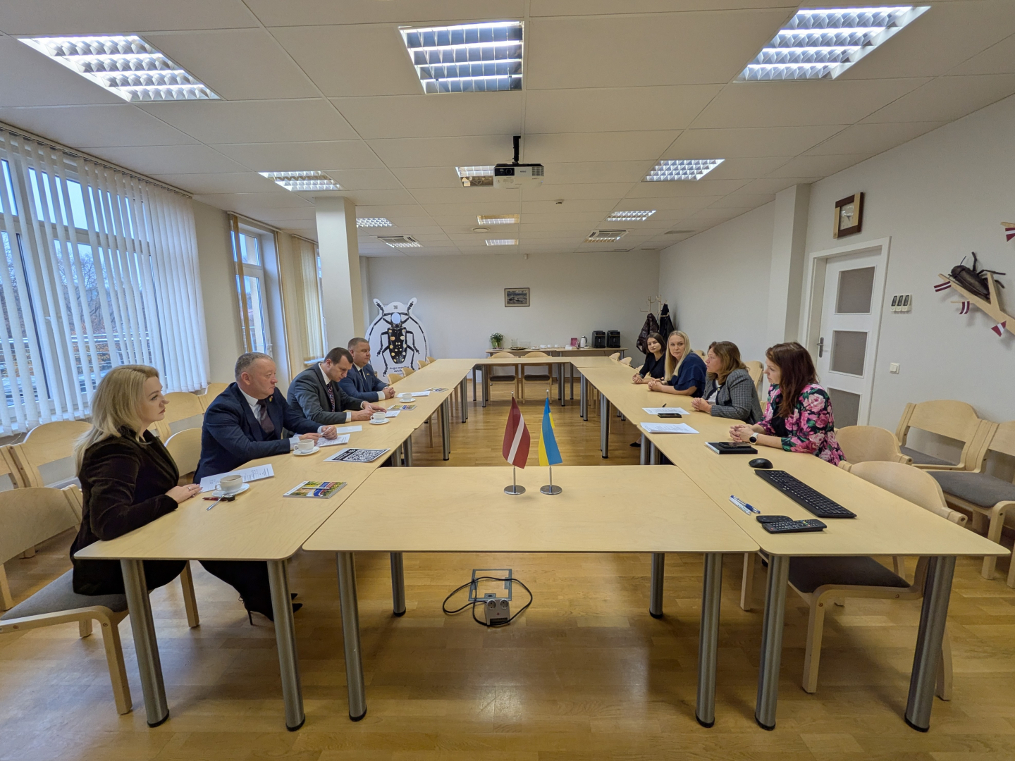 Sanāksmju telpa, U veida galds, 8 cilvēki no abām pusēm sēž pie galda