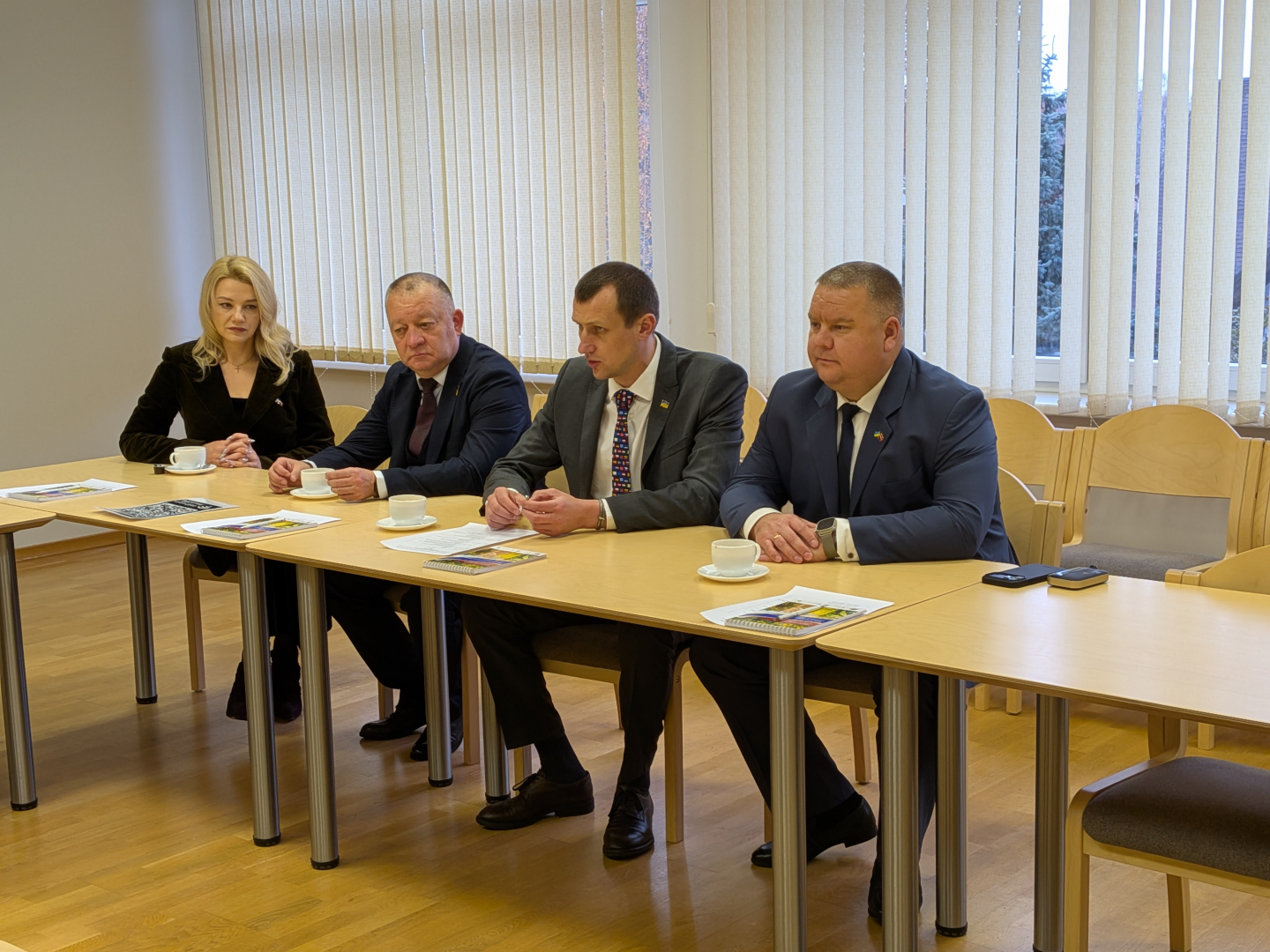 Ukrainas delegācija 4 cilvēki sēž sanāksmes zālē pie galda 