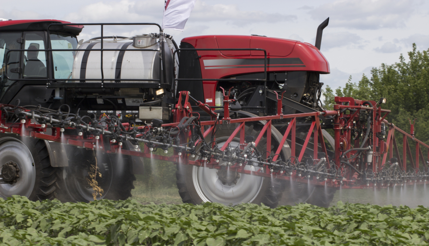 Foto sarkans traktors, pietuvinātas spraulas, kas smidzina migliņu uz augiem