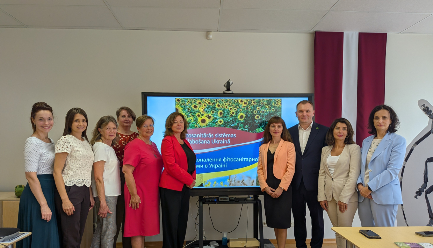 Grupas bilde: 6 cilvēki no labās (LV) puses un 4 cilvēki no kreisās (UA), fonā LV karogs un ekrāns